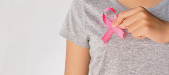 Woman in gray shirt holding pink ribbon to support breast cancer